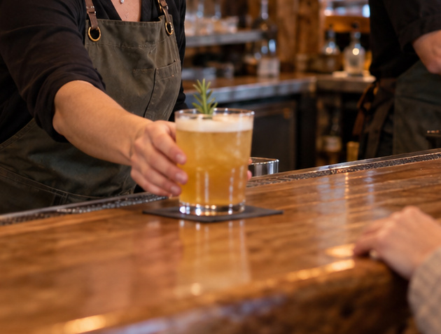 An amber drink being served across a timber bar